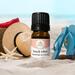 Bottle of Beach Vibes Essential Oil Blend by Whole Self Aromatherapy on a beach with beach hat, flip flops, sunglasses alongside of it.